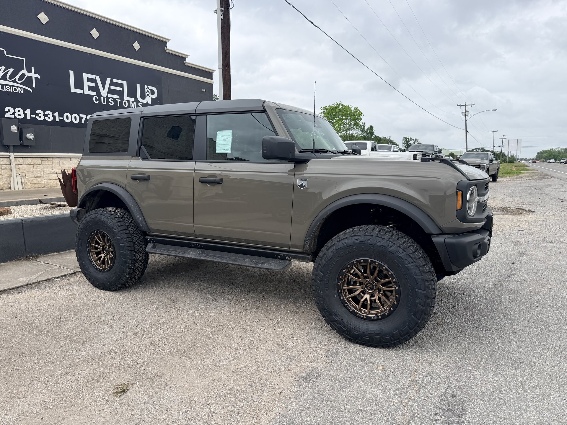 Olive Ford Bronco lifted with bronze wheels in front of Level Up Customs shop, Alvin TX